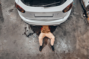 Mechanic lying and working under car at the repair garage.