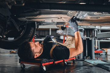 Concentrated auto mechanic male working alone on the floor repairing bottom of the car, look at details, troubleshoot the car.
