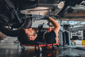 Male car mechanic worker working using wrench tool for repair, maintenance underneath car. Mechanic vehicle service checking under car in garage.