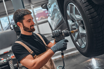 Professional car mechanic changing car wheel at car maintenance and auto service garage.