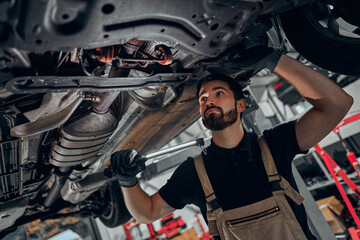 Mechanic examining under the car at the repair garage. - obrazy, fototapety, plakaty
