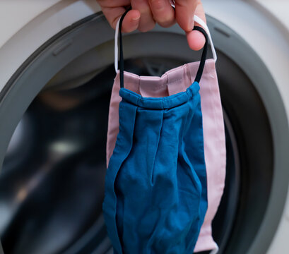 Hand Putting Used Cloth Face Masks Into A Washing Machine. 