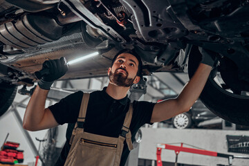 Professional auto mechanic working on the undercarriage of a car. - obrazy, fototapety, plakaty