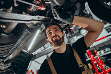 Portrait of car mechanic working with tools under car in automobile at repair service shop.