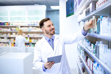 Naklejka na ściany i meble Professional handsome male pharmacist working in pharmacy store or drugstore. Taking medicines of the shelf. Healthcare and apothecary.