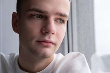 portrait of a sad pensive guy at the window close-up