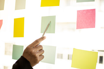 Business men are writing on a post-it that is placed in the glass of the conference room to brainstorm the ideas of the operations of the company together to grow the business. business concept.