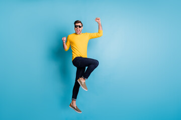 Full size profile photo of impressed handsome guy jumping fists up celebrate isolated on blue color background