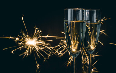 Two glasses of champagne with sparklers in background. New Year's Eve celebration. - obrazy, fototapety, plakaty