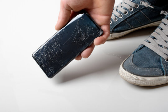 A man takes a broken smartphone from the ground. Damaged mobile phone with cracked touch screen.