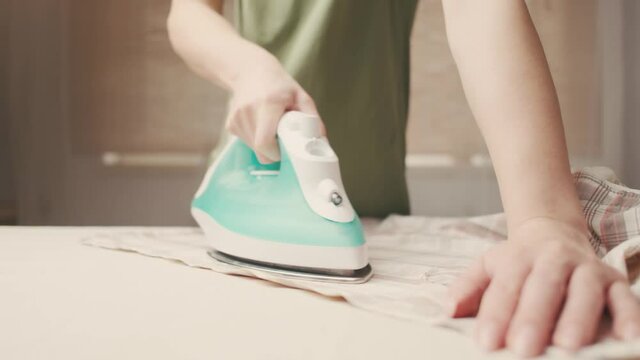 Unrecognizable woman ironing her shirt at home.
