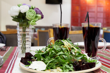served green salad and bouquet of artificial flowers in vase on table in cafe with blurred background