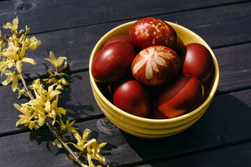 Red Easter eggs in a yellow bowl on a black wooden background.