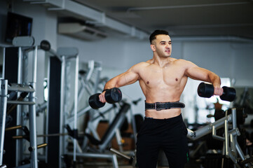 Obraz na płótnie Canvas Muscular arab man training in with dumbbells modern gym. Fitness arabian men with naked torso doing workout .