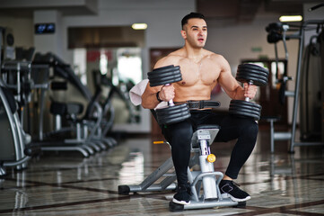 Muscular arab man training in with dumbbells modern gym. Fitness arabian men with naked torso doing...