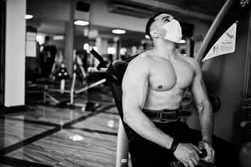 Naklejka premium Muscular arab man, wear medical face mask training in modern gym. Fitness arabian men with naked torso doing exercises, durig coronavirus pandemic.