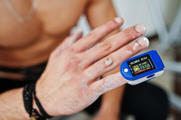 Close up pulse oximeter in finger in fitness men with naked torso.