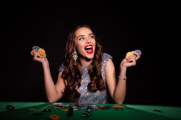 Photo of amazed excited young lady hold poker chips sit table luck winner rich money isolated on...