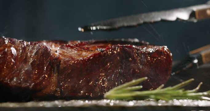 Close up shot of a juicy grilled steak on chef's preparation table. Smoke rising from big piece of tasty meat.