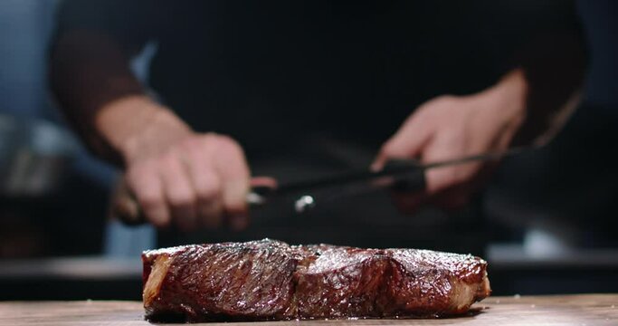 Chef sharpening his knife in front of raw steak. Chef preparing his cooking knife for cutting meat on kitchen table