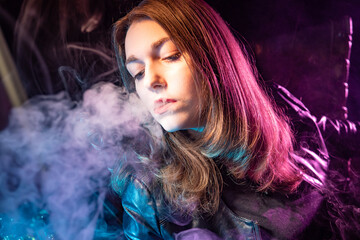 A blower blows smoke. Vaper blows smoke from his lips. Woman lets out smoke from her mouth. Concept is the pleasure of smoking. A student smokes an electronic cigarette. Vaper on a dark background