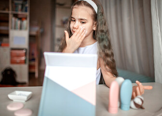 Beautiful teenage girl watching beauty master class with tablet online and doing spa procedure by herself, kid with smooth mask on face, beauty salon at home - Powered by Adobe