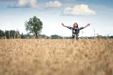 Teenage girl stands with arms up in the wheat field in summer day