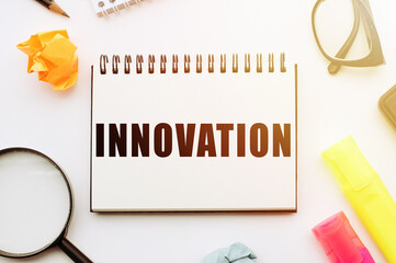 Text INNOVATION in notebook on white table with office tools.