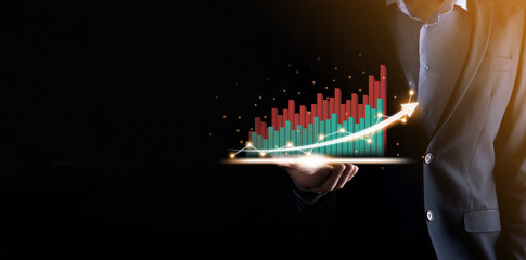 Businessman holding and showing a growing virtual hologram of statistics, graph and chart with arrow up on dark background. Stock market. Business growth, planing and strategy concept.