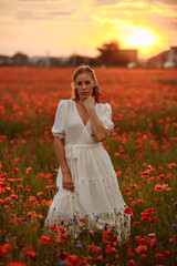 girl in a white dress in a field of poppies on a sunset background