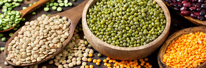 Different legumes. Mung beans, red  beans, lentils, peas and chickpeas in wooden bowls on a brown wooden kitchen table. Beans close-up. Vegetarian food. Banner
