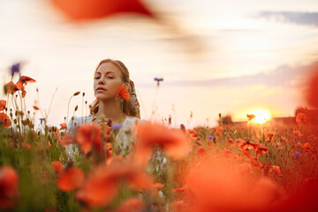 Obraz na płótnie Canvas girl in a white dress in a field of poppies on a sunset background
