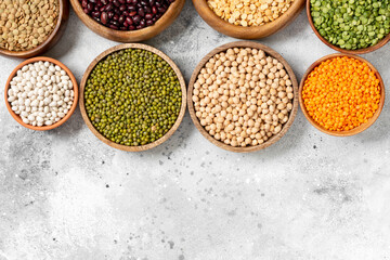 Different legumes. Mung beans, red and white beans, lentils, peas and chickpeas in wooden bowls on the light grey kitchen table. Vegetarian food. Top view with copyspace