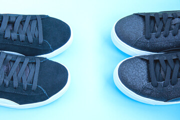 Two pairs of black sneakers on blue neon background. Concept of healthy lifestyle, everyday training. Shoes for women's training. Flat lay
