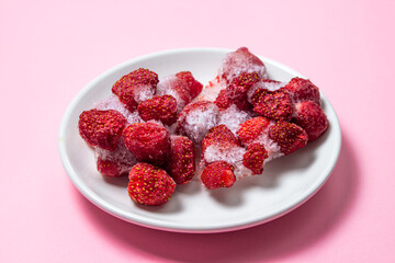 Frozen strawberries on a white plate. Strawberries in ice on a pink background. Frozen berries.