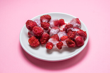 Frozen strawberries on a white plate. Strawberries in ice on a pink background. Frozen berries.