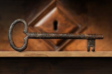 Extreme closeup of an old and vintage rusty key on a wooden shelf with a wood keyhole on background. Photography.