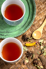 Aerial view of two blue cups with tea, wooden spoon, on green plate and braided tray, in vertical