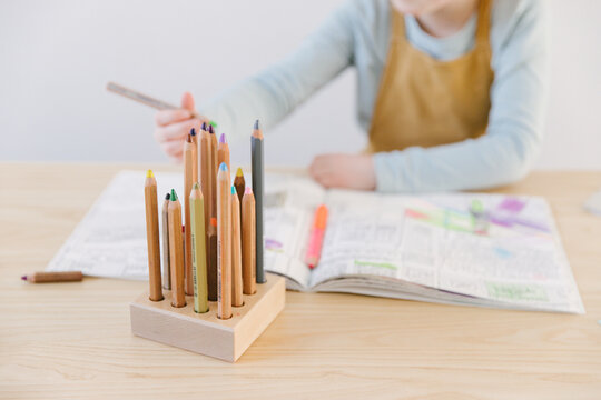 4 year old girl is drawing in her coloring book with thick waldorf style wooden pencils.