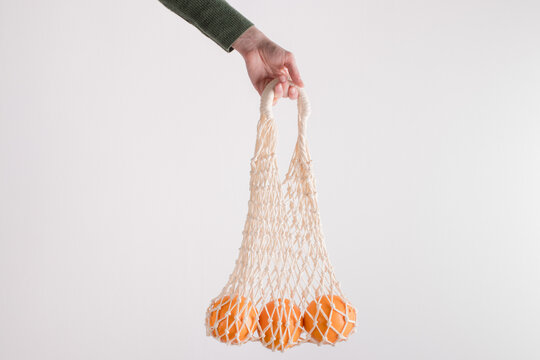 Mesh bag with oranges in female hand. Modern reusable shopping, zero waste concept.