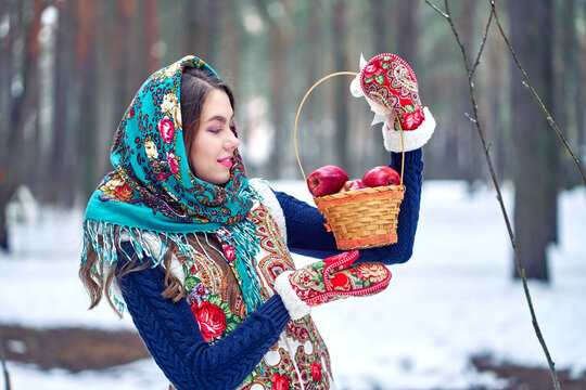Russian woman in national costume with a basket of apples. Winter background.