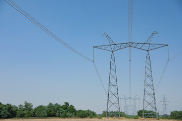 High voltage towers with electricity transmission power lines in field on sunny day