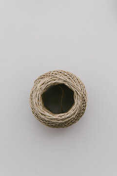 A rolled up ball of thin natural rope seen from the top on a light grey empty table.