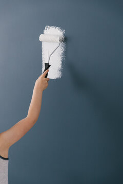 A kid rolling white paint on a dark blue wall helping out while redecorating.