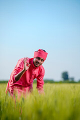 Naklejka na ściany i meble Young indian farmer standing at green wheat field on sky background
