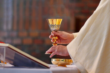 Chalice in the hands of the priest on the altar during the celebration of the mass - obrazy, fototapety, plakaty