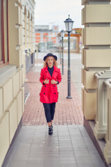 young woman near an office building with vintage street lamps in a red jacket and hat
