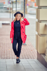 young business woman near office building in red coat and hat. vertical