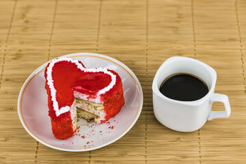 Red cut cake on a saucer and a cup of coffee on a bamboo napkin. Top view with copy space.