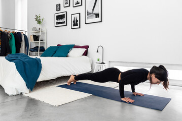 Fit woman practicing Chaturanga pose during yoga training session at modern bedroom